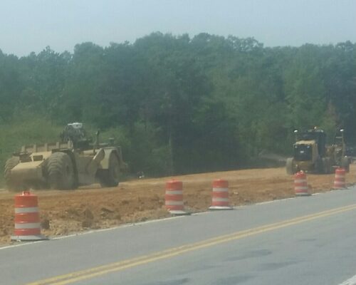 Construction vehicles operating near traffic cones and barriers on a road.