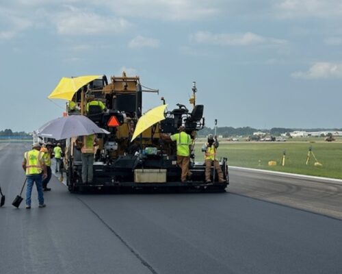 A paving crew applying fresh asphalt to a road while operating heavy machinery.