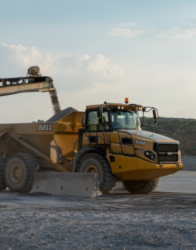 Construction vehicles working on a rural road surrounded by open fields.