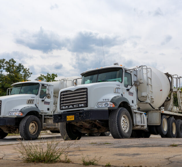 Two cement trucks parked side by side on a gravel road.