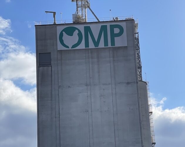 The OMP cement silo standing tall against a bright blue sky with clouds in the background.